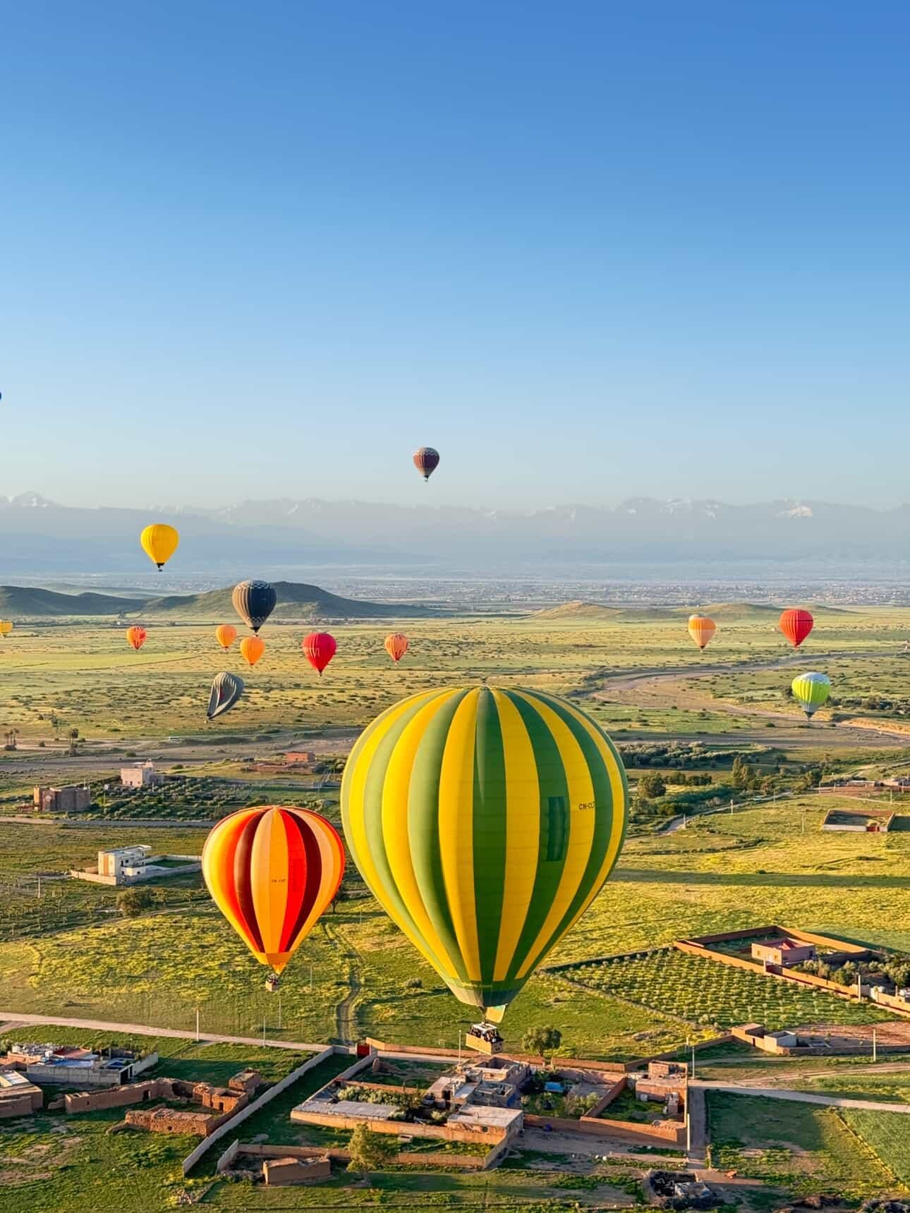 Hot air balloons over green fields and villages near Marrakech with the snowy Atlas Mountains
