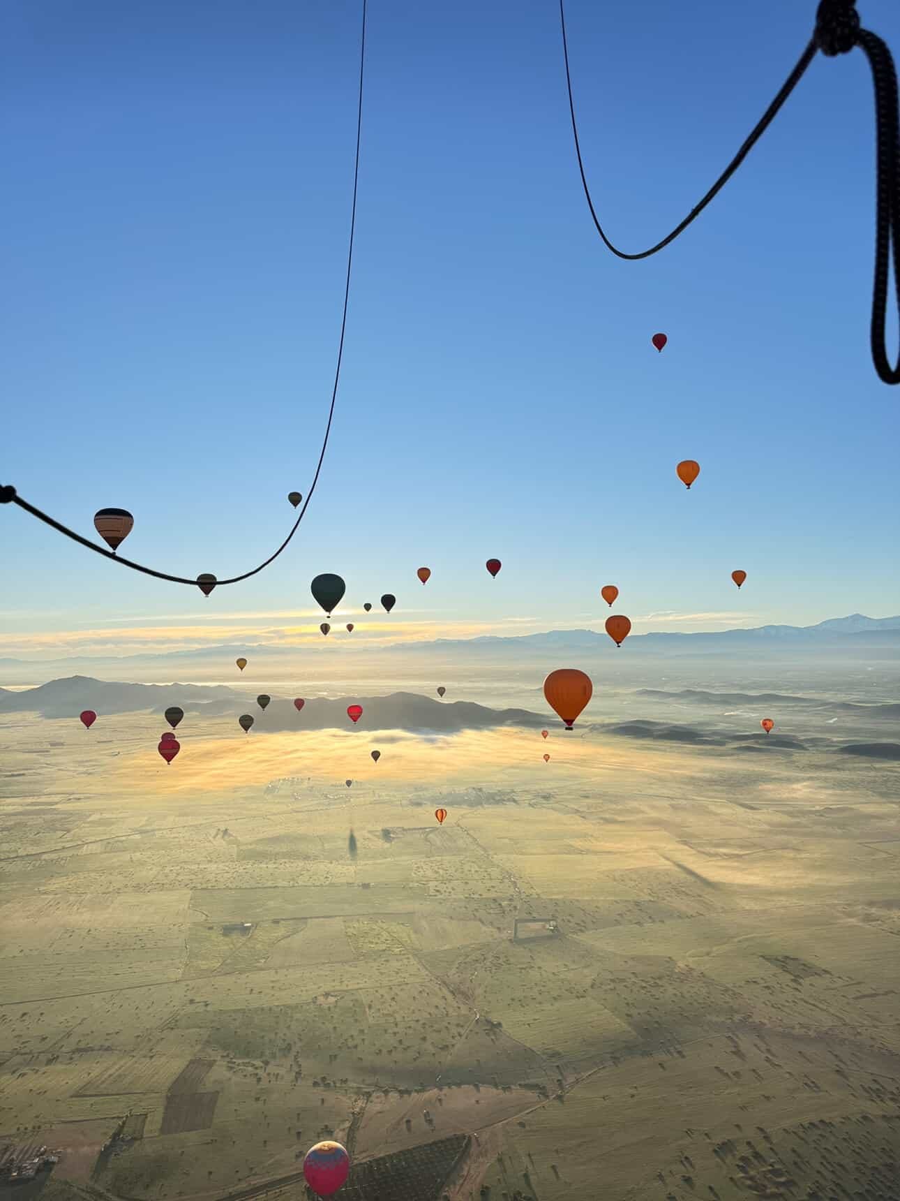 Hot air balloons over misty fields near Marrakech at sunrise, seen from a balloon basket