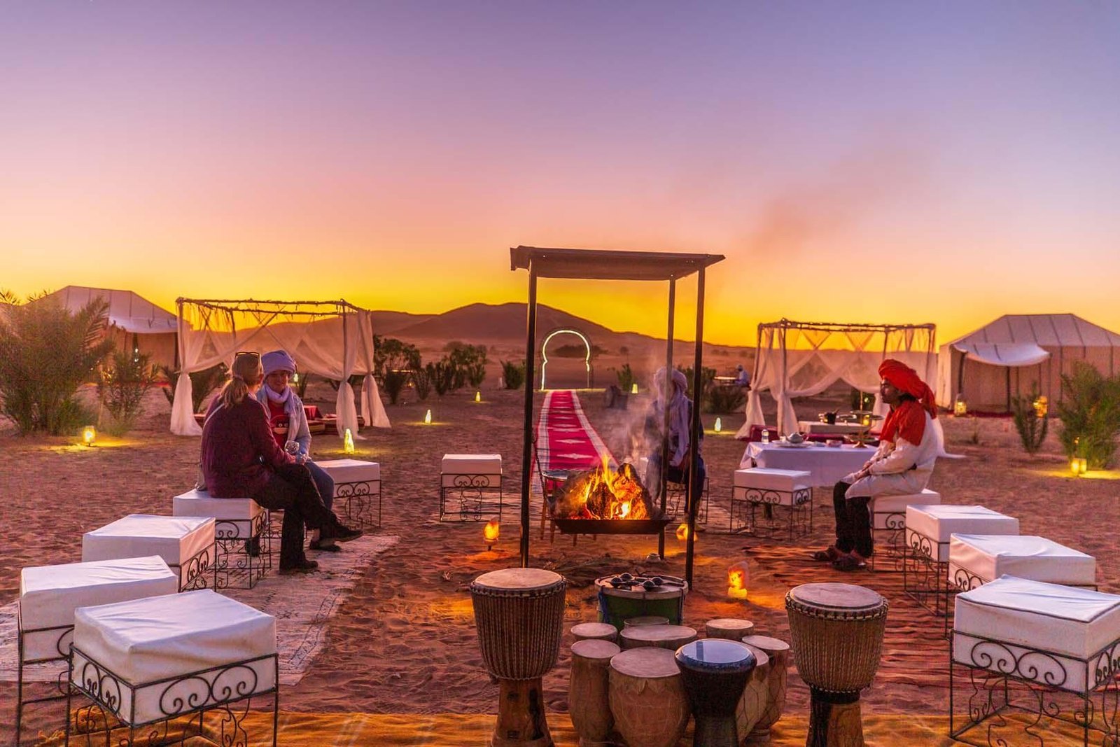 Luxury desert camp in the Sahara at sunset, with a fire, drums and canopy lounges on a Morocco luxury tour